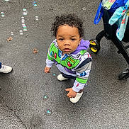 Kyyeer is registered to the contest to win money with this photo: blanket, blue_bag, bubbles, buzz_lightyear, casual_clothing, child, curious, curly_hair, cute, hoodie, looking_up, outdoor, person, playful, sidewalk, small_child, stroller, toddler, wet_pavement, white_shoes