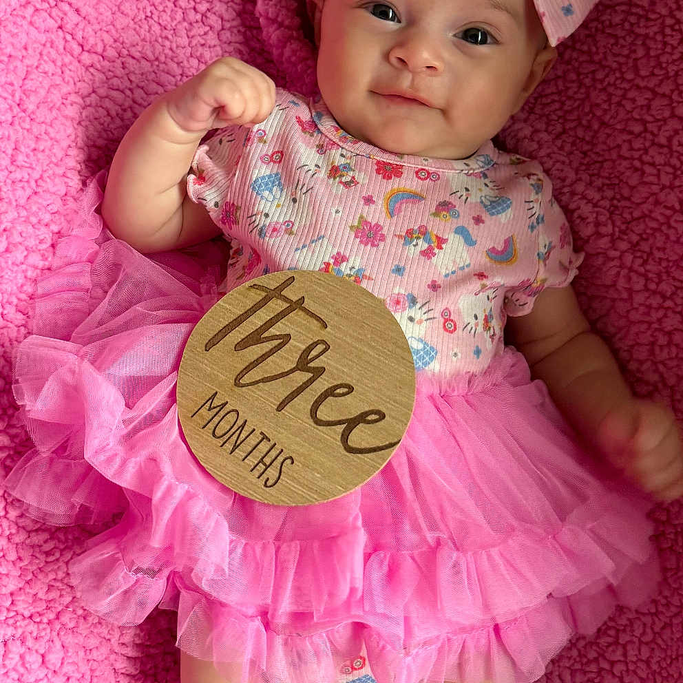 Nakiyah is registered to the contest to win money with this photo: baby, blanket, child, clothing, cute, floral, girl, happy, headband, infant, lying_down, milestone, pink, portrait, skin, small, smiling, soft, tutu, wooden_sign