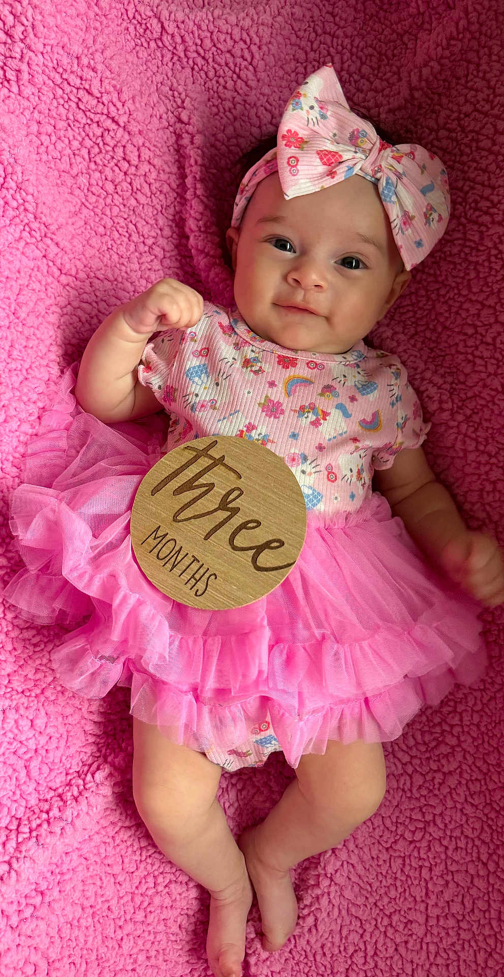 Nakiyah is registered to the contest to win money with this photo: baby, infant, girl, pink, tutu, headband, floral, blanket, soft, cute, milestone, wooden_sign, smiling, lying_down, clothing, portrait, child, happy, skin, small