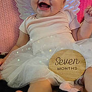 Jaycee joined the competition — help win amazing prizes! baby, infant, child, smiling, happy, angel_costume, wings, headband, flower, tutu, dress, milestone, seven_months, portrait, lying_down, indoor, pink_blanket, wooden_sign, bare_feet, celebration