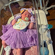 Jordyn joined the competition — help win amazing prizes! newborn, baby, hospital_bassinet, pacifier, purple_dress, mittens, headband, plush_toy, blanket, socks, infant, sleeping, clothing, baby_care, medical_equipment, wooden_floor, person, cute, indoor, portrait