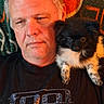 man, dog, puppy, black_tshirt, sitting, shoulder, indoor, portrait, fluffy, pet, animal, casual, relaxed, colorful_background, expression, hair, face, companion, cute, domestic_animal