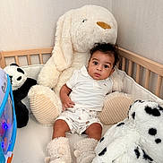 Kayden a rejoint le concours — aidez-le/la à gagner de superbes lots ! baby, crib, plush_toy, stuffed_animal, dog_toy, panda_toy, white_clothing, baby_booties, indoor, child, cute, soft_toys, curly_hair, infant, wooden_crib, light_wall, play_area, toddler, sitting, comfortable