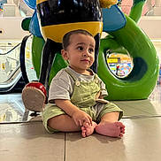 Muhammad joined the competition — help win amazing prizes! toddler, child, barefoot, overalls, striped_shirt, sitting, indoor, statue, bee_statue, colorful, green, yellow, red, floor, tiles, mall, playful, curious, young_child, sculpture