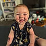 arm, baby, background, bookshelf, child, clothing, cute, expression, face, furniture, happy, indoors, person, room, sitting, skin, smiling, tattoo, television, toy