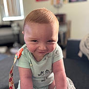 Wesley is registered to the contest to win money with this photo: arms, baby, blurred_background, cheeky, child, cute, expression, face, furniture, head, home, indoors, infant, onesie, person, playful, seated, skin, smiling, soft_focus