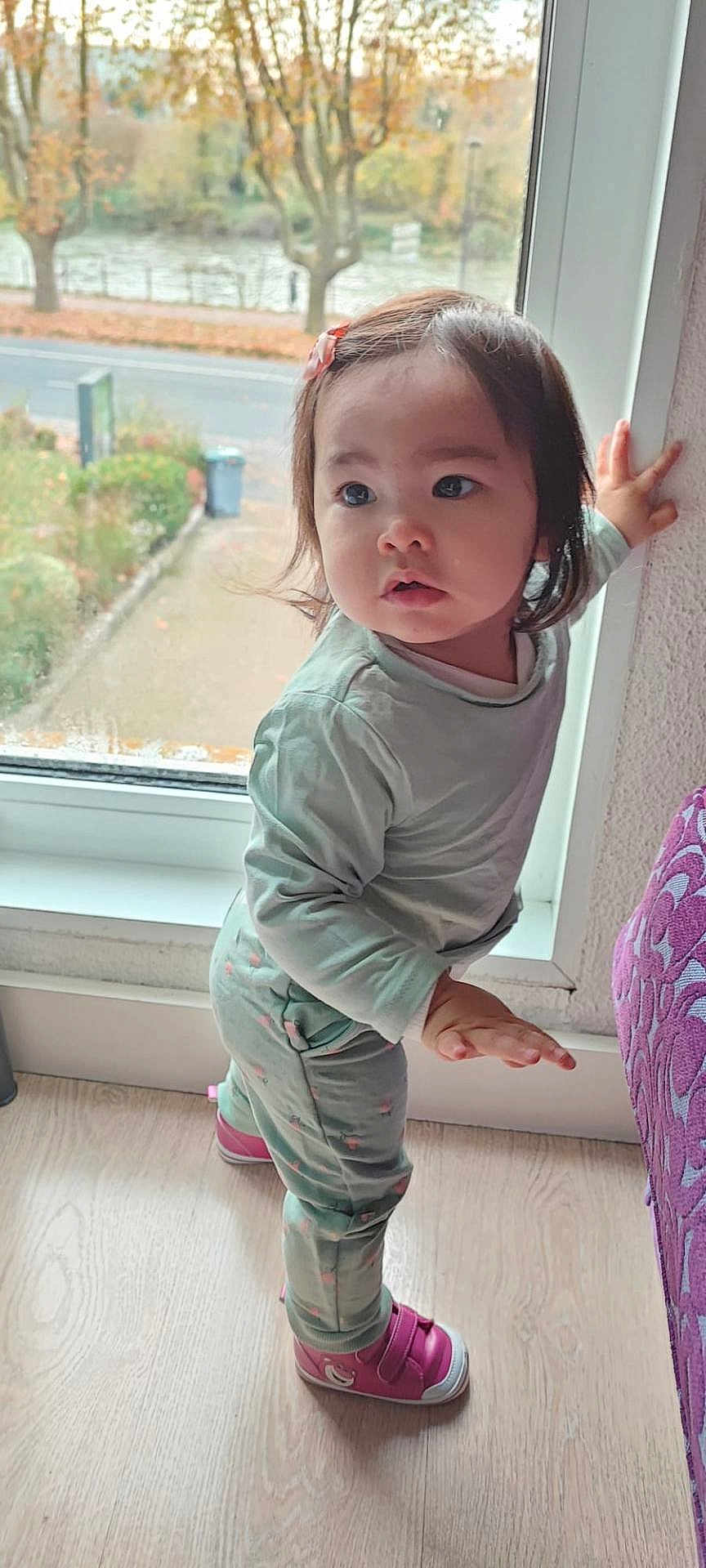 Luciana participe au concours pour gagner de l'argent avec cette photo : toddler, child, indoor, window, curious, standing, pajamas, pink_shoes, hair_clip, wooden_floor, autumn, trees, leaves, street, daylight, person, young_child, balance, home, casual_clothing