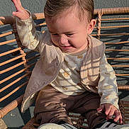 Liam Santos joined the competition — help win amazing prizes! child, toddler, baby, sitting, chair, woven_chair, portrait, outdoor, sunlight, shadows, smiling, happy, face, hair, clothing, vest, pants, sneakers, raised_hand, casual