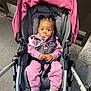 baby, stroller, pacifier, pink_clothing, sneakers, child, urban, sidewalk, cute, infant, hair_buns, jacket, pants, sitting, outdoor, person, footwear, seat_belt, expression, young_child
