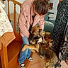 blue_jeans, bun, couch, cuddle, decorations, dog, furniture, german_shepherd, home, hugging, indoors, long_hair, person, pillows, pink_jacket, portrait, sneakers, staircase, tile_floor, wall_art