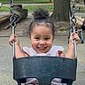toddler, child, swing, playground, outdoor, happy, smile, curly_hair, park, chains, black_swing, summer_clothing, young_child, holding_on, fun, recreation, trees, daylight, casual_wear, joy