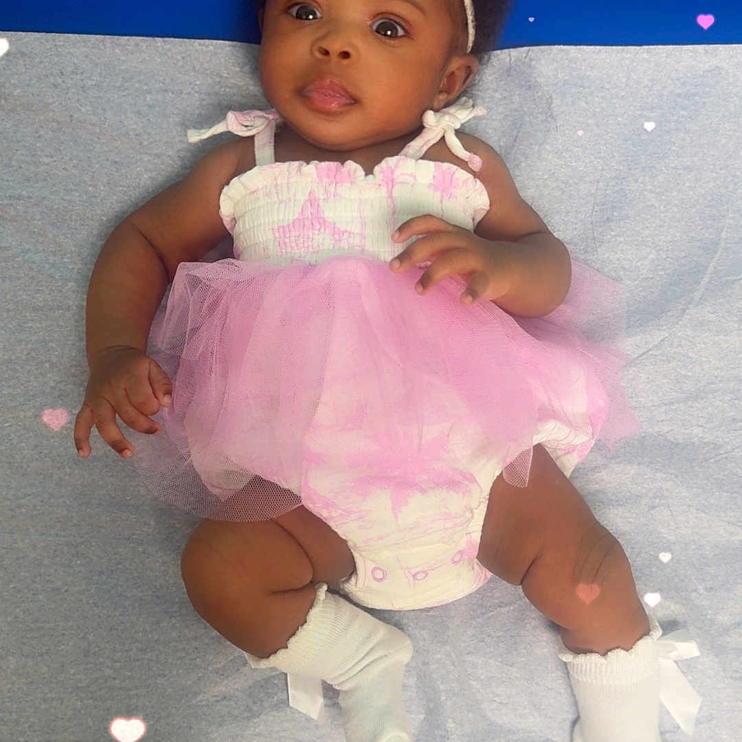 Tyniyah is registered to the contest to win money with this photo: baby, infant, girl, pink_tutu, headband, socks, lying_down, curious_expression, blue_background, hearts_overlay, cute, child, portrait, soft_lighting, adorable, clothing, floor, skin, closeup, happy