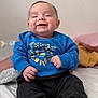 baby, smiling, blue_sweater, pasta_illustration, sitting, bed, blanket, pillow, happy, infant, clothing, person, indoors, cute, portrait, child, soft_toys, cozy, casual, relaxed