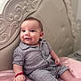 baby, infant, striped_clothing, bed, pink_bedspread, headboard, ornate_furniture, carving, bracelet, happy, curious, portrait, indoor, child, person, sitting, closeup, cute, smile, soft_lighting