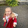 child, girl, smiling, outdoor, coat, hoodie, backpack, gravel, blue_eyes, long_hair, building, bush, steps, door, casual_clothing, footwear, portrait, happy, person, daylight