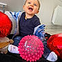 Malône a rejoint le concours — aidez-le/la à gagner de superbes lots ! toddler, child, blue_eyes, smiling, indoor, balloon, red_balloon, pink_ball, toy, plaid_shirt, navy_shirt, socks, floor, tile_floor, blanket, happy, playful, person, cute, joyful