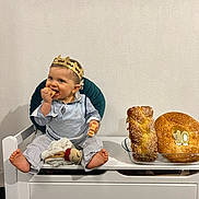 Malône a rejoint le concours — aidez-le/la à gagner de superbes lots ! baby, child, crown, toy, bench, bread, celebration, snack, blue_eyes, happy, indoor, white_wall, clothing, foot, sitting, smile, face, food, party, cute