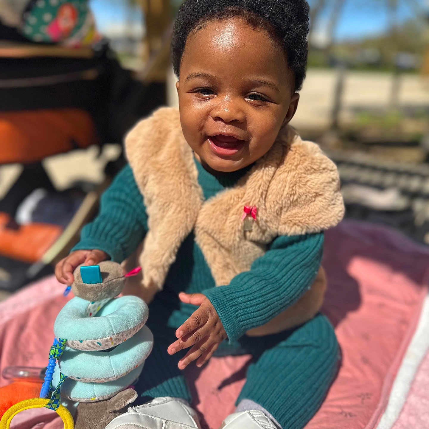 Tessy a rejoint le concours — aidez-le/la à gagner de superbes lots ! baby, child, smiling, outdoor, toy, blanket, vest, knitwear, happy, sitting, face, person, footwear, sunlight, play, infant, cute, colorful, warm_clothing, portrait