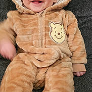 Xavier is registered to the contest to win money with this photo: baby, child, smiling, onesie, hood, ears, plush_toy, couch, fuzzy_clothing, cute, infant, happy, portrait, indoor, soft_texture, cozy, brown, face, person, seated