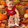 baby, child, smiling, portrait, autumn, fall, pumpkins, hay_bale, flowers, leaves, outdoor, seasonal, headband, bow, red_outfit, patterned_clothing, sitting, blanket, rustic, happy
