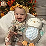 Anna is registered to the contest to win money with this photo: baby, child, infant, smiling, happy, portrait, indoors, christmas_tree, holiday, lights, ornaments, headband, bow, floral_clothing, onesie, socks, stuffed_animal, plush_toy, owl_toy, blanket