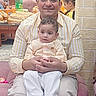 man, child, toddler, indoor, balloons, bread, table, family, smile, clothing, striped_shirt, pants, curly_hair, celebration, people, seated, wall, mirror, decor, happy