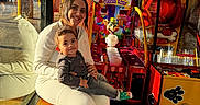 Augustine joined the competition — help win amazing prizes! arcade_game, bench, casual_clothing, child, colorful, family, game_machine, happy, indoor, joy, leisure, person, playful, reflection, seated, smile, sunlight, toddler, window, woman