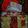 Kaylee is registered to the contest to win money with this photo: baby, child, christmas, holiday, santa_hat, gift_box, wrapped_present, tree, decorations, festive, cute, peek, smile, indoors, celebration, red, green, plaid, winter, joy