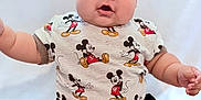 Junior is registered to the contest to win money with this photo: arms_outstretched, baby, black_shorts, child, chubby, clothing, curious, cute, expression, indoor, infant, mickey_mouse, person, plump_legs, portrait, shirt, sitting, skin, smiling, white_background