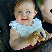 Clémence participe au concours pour gagner de l'argent avec cette photo : baby, child, blue_eyes, smiling, stroller, toy, white_collar, cute, portrait, infant, hand, face, outdoor, person, seatbelt, closeup, skin, expression, happy, young