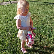 Julie a rejoint le concours — aidez-le/la à gagner de superbes lots ! blonde_hair, bunny, child, cute, daylight, girl, grass, greenery, happy, outdoor, pink_shoes, playground, smiling, standing, stuffed_toy, summer, sunlight, swing, toy, white_outfit