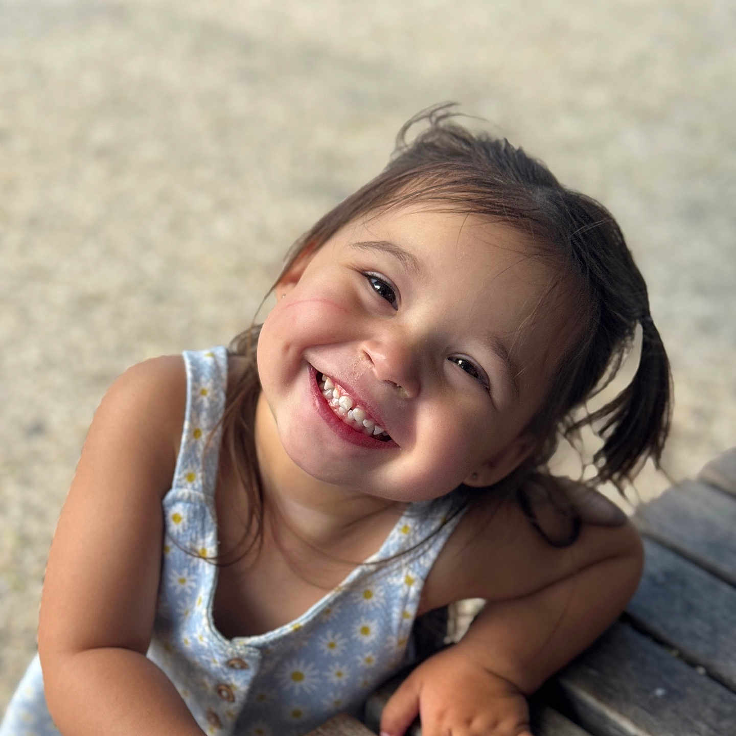 Fallone participe au concours pour gagner de l'argent avec cette photo : casual, cheerful, child, closeup, cute, daisy_pattern, dress, face, hand, happy, natural_light, outdoor, person, pigtails, portrait, skin, smiling, toddler, wooden_table, young_child