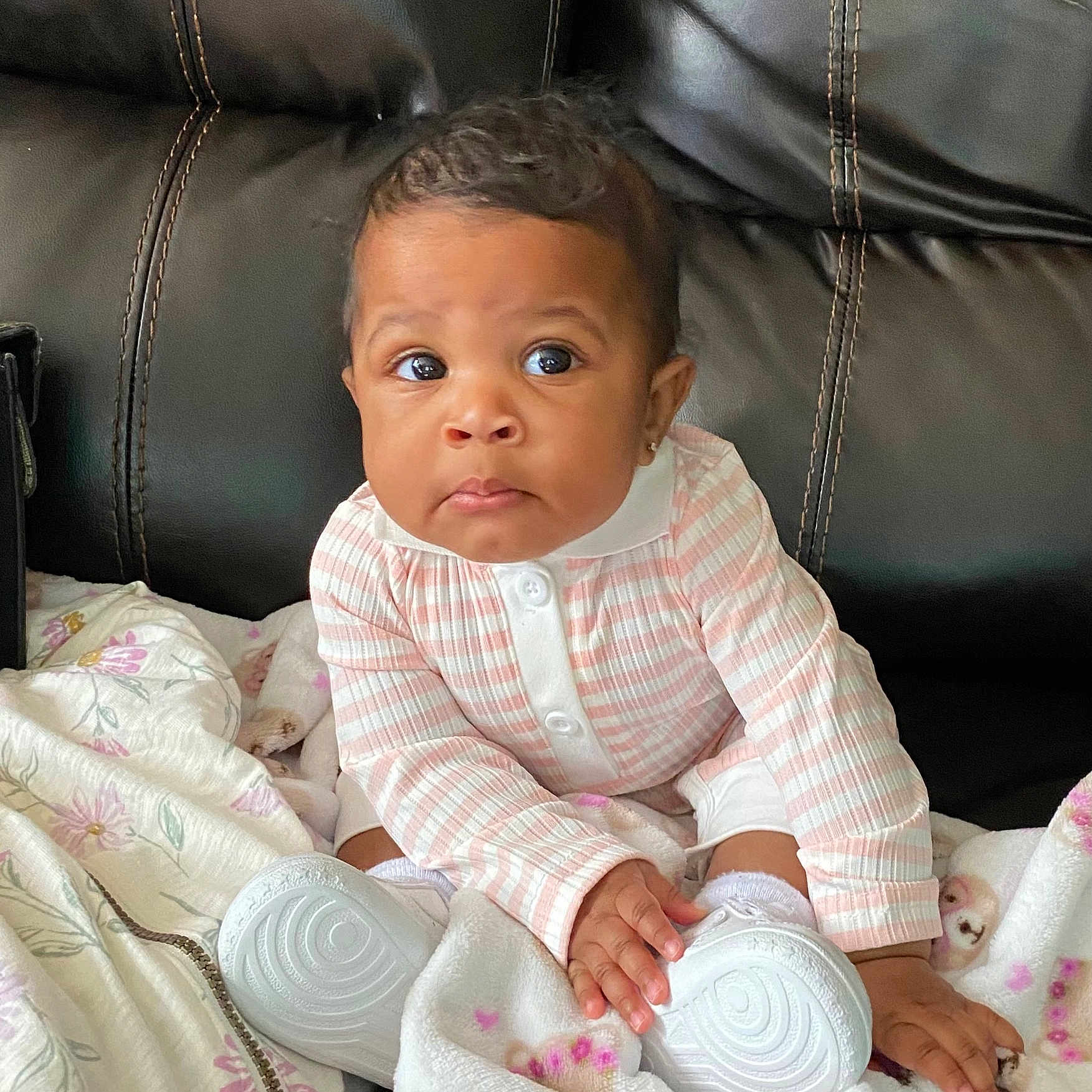 Jailani is registered to the contest to win money with this photo: baby, blanket, child, couch, cozy, curious, expression, face, hand, indoors, infant, leather, pink, portrait, shoe, sitting, striped_clothing, white, white_shoe, young_child