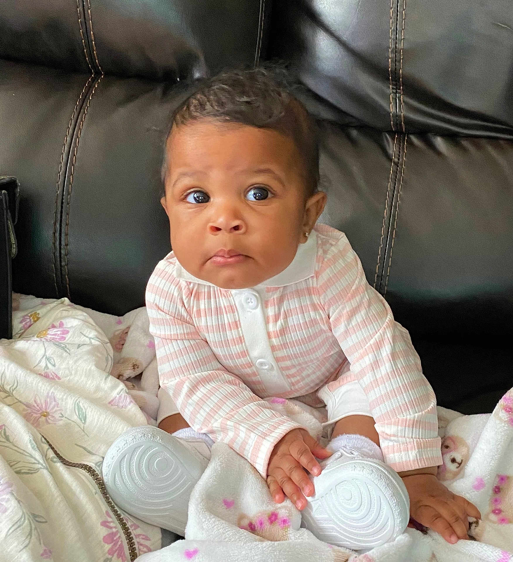 Jailani is registered to the contest to win money with this photo: baby, child, infant, sitting, blanket, shoe, white_shoe, striped_clothing, pink, white, couch, leather, hand, face, expression, curious, indoors, portrait, young_child, cozy