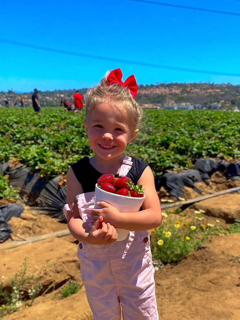 River is registered to the contest to win money with this photo: agriculture, farmer, field, flower, fun, grass, grassland, happy, hat, joy, landscape, leisure, people_in_nature, person, plant, plantation, sky, smile, soil, toddler