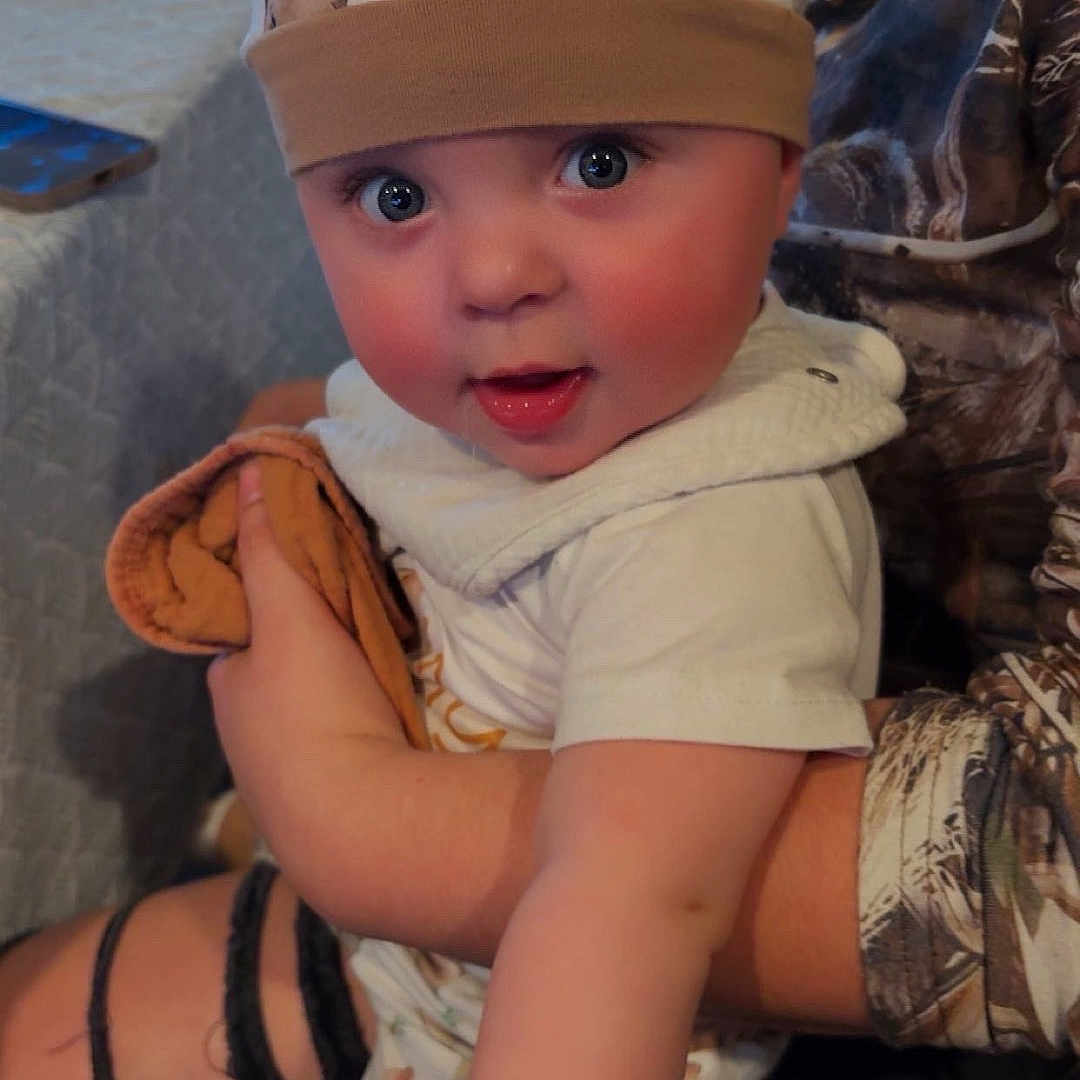 Hudson is registered to the contest to win money with this photo: accessories, baby, baseballcap, bodypart, cap, clothing, dress, electronics, face, finger, hand, hat, head, jewelry, mobilephone, necklace, pants, person, photography, portrait