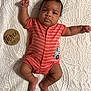 baby, infant, three_months, onesie, striped_clothing, raised_arm, lying_down, quilt, textured_bedspread, wooden_sign, curious_expression, cute, child, newborn, indoors, soft_lighting, skin, foot, hand, face