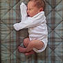 Silas joined the competition — help win amazing prizes! baby, newborn, infant, white_onesie, plaid_mattress, sleeping, curled_up, soft_texture, cute, small_feet, peaceful, indoors, portrait, child, resting, bed, fabric, patterned, cozy, lying_down