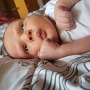Silas is registered to the contest to win money with this photo: baby, infant, face, hands, blanket, bottle, baby_lotion, close_up, lying_down, pattern, room, soft_light, curious, skin, person, newborn, indoors, expression, resting, pillow