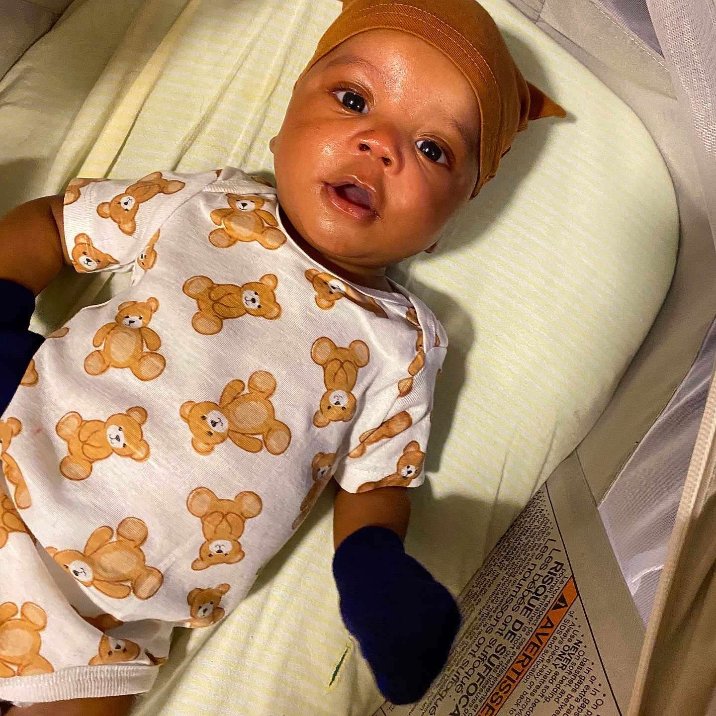 Kai Green joined the competition — help win amazing prizes! baby, bed, child, clothing, comfort, crib, cute, face, hat, indoor, infant, looking_up, mittens, portrait, sleeping_area, sleepwear, soft_lighting, teddy_bear_pattern, textile, young_child