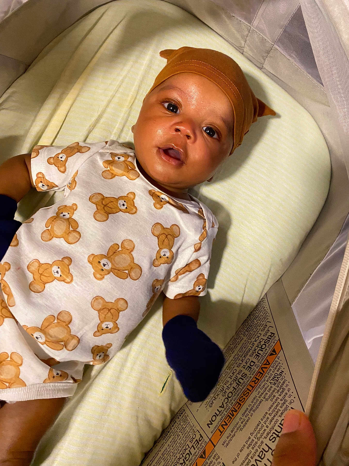 Kai Green joined the competition — help win amazing prizes! baby, infant, crib, hat, mittens, teddy_bear_pattern, clothing, sleeping_area, bed, face, child, cute, looking_up, young_child, comfort, textile, sleepwear, soft_lighting, indoor, portrait