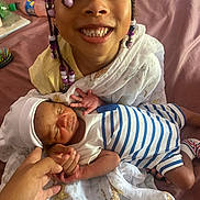 Simone Garrett is registered to the contest to win money with this photo: child, newborn, baby, smiling, holding, blanket, bed, hair_beads, family, happy, infant, person, sleeping, white_clothing, striped_clothing, hand, indoor, skin, face, portrait