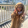 child, glasses, costume, bear, hood, porch, railing, sunlight, smile, peace_sign, outdoor, residential, daylight, carpet, shadow, house, street, person, happy, cute