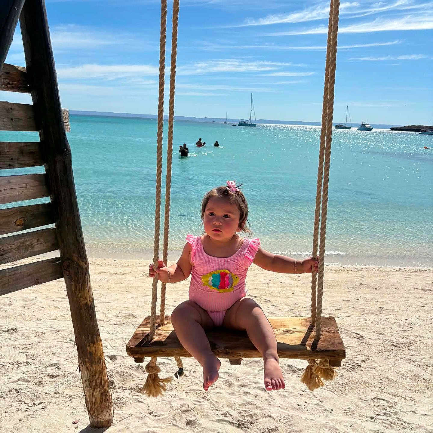 Naylan joined the competition — help win amazing prizes! toddler, child, swing, beach, sand, ocean, sea, sky, clouds, rope, wood, swimsuit, sunny, vacation, water, boats, outdoor, summer, play, holiday