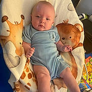 Lukas joined the competition — help win amazing prizes! baby, infant, onesie, blanket, giraffe, bear, animal_print, cute, child, face, smiling, furniture, indoors, person, blue_clothing, soft_texture, lying_down, young_child, happy, cozy