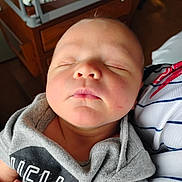 Troy is registered to the contest to win money with this photo: baby, sleeping, hoodie, grey_clothing, infant, face, peaceful, resting, person, portrait, closeup, newborn, child, soft_light, indoor, fabric, striped_clothing, cute, calm, skin