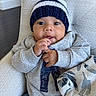 baby, blanket, blue_clothing, chair, child, cozy, curious, cushion, finger_nibbling, gray_clothing, hat, indoors, infant, looking_at_camera, pom_pom, portrait, sitting, sweater, textile, winter_clothing