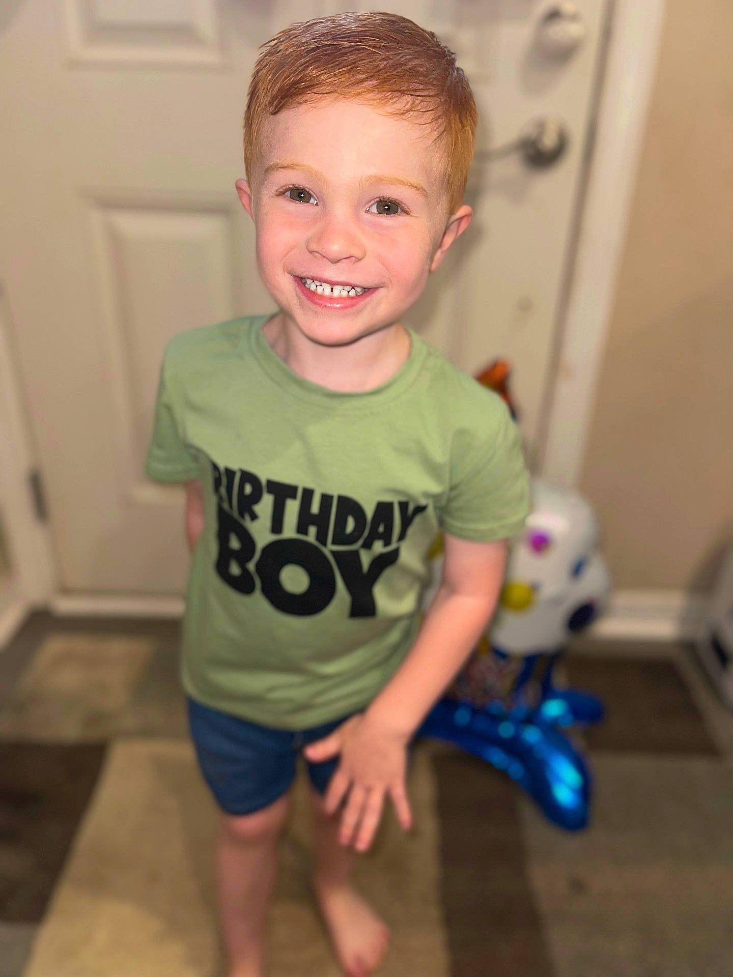 Blake is registered to the contest to win money with this photo: barefoot, birthday, boy, carpet, casual_clothes, celebration, child, cute, door, front_view, green_shirt, happy, human, indoor, person, portrait, red_hair, shorts, smiling, young