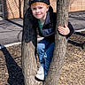 baseball_cap, boy, brick_wall, cap_backwards, casual_clothing, child, hands, jeans, nature, outdoor, peeking, playground, portrait, red_hair, shadow, smile, sneakers, sunlight, tree, tree_trunk