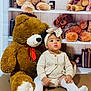 baby, child, teddy_bear, stuffed_animal, sitting, headband, white_socks, knitwear, toy, shelf, books, indoor, cute, portrait, childhood, soft_toy, floor, curly_hair, red_ribbon, decor